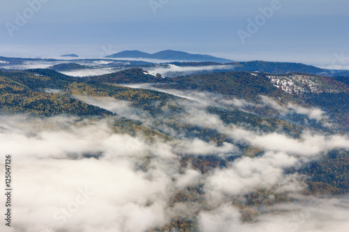 Landscape in autumn mountains. View from the top of the mountain on the forest fog coatings and village in the valley. Carpathians. Europe.