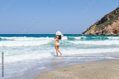 Beautiful tanned brunette in white bikini walking on the beach