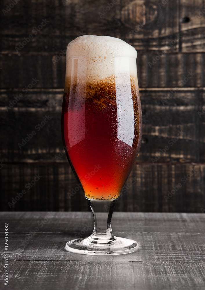 Glass of brown ale beer with foam on wood