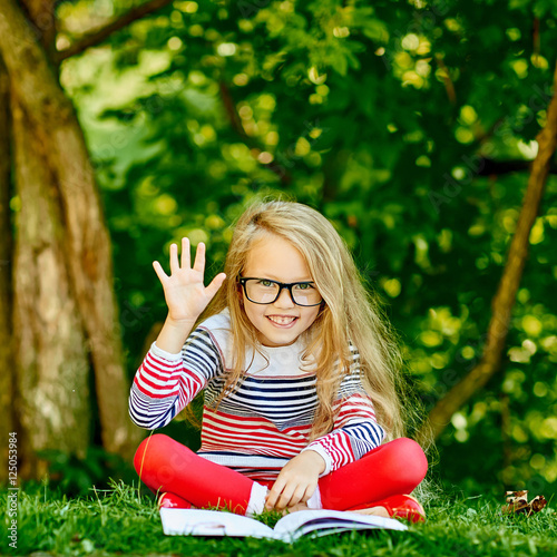 Cute little girl with a book in summer park showing five fingers photo