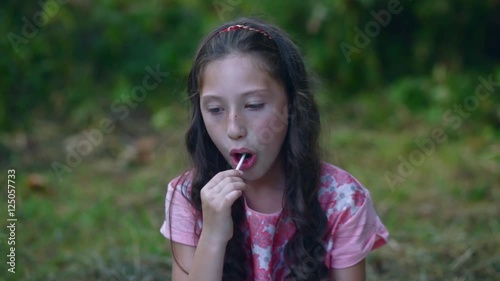 Beautiful little girl eating a lollipop candy in the garden.