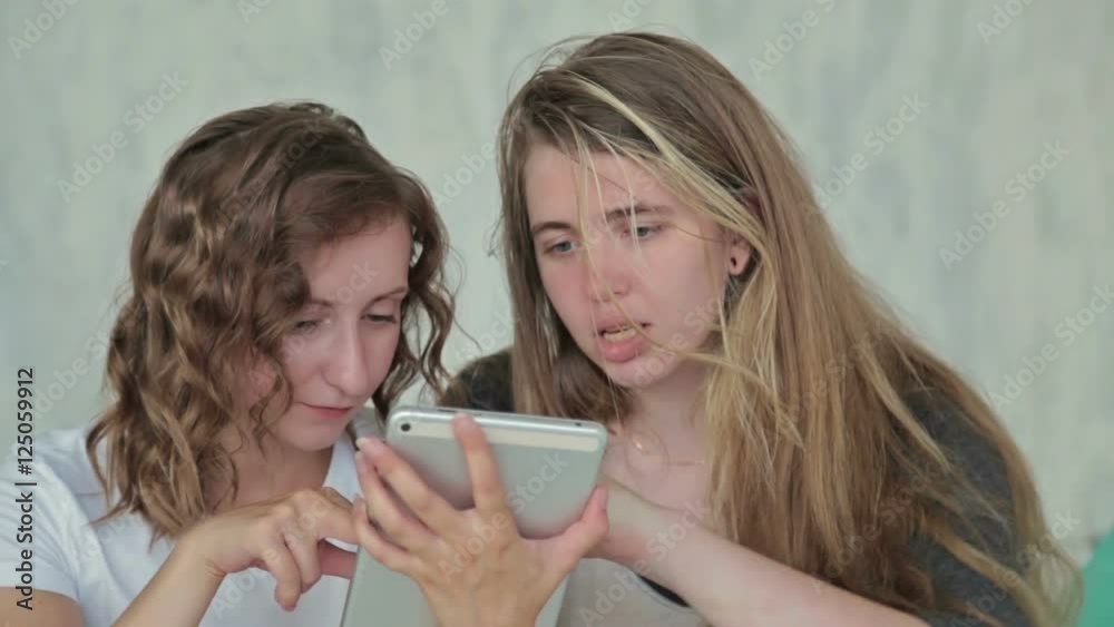 Two women sitting on bed, talking and using digital tablet. Friendship and technology concept Two women sitting on bed, talking and using digital tablet. Friendship and technology concept