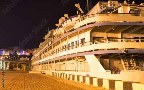 Old passanger vessel is moored alongside the pier/jetty at port of Odessa, Ukraine. Colorful lights are on background. Night view picture
