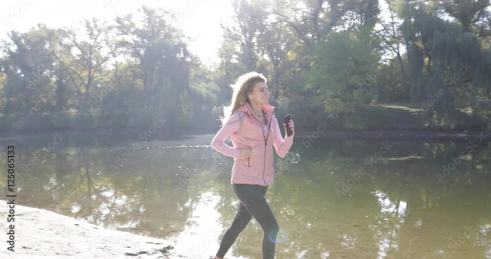 Woman run river active fitness female runner exercising outdoor sport using headphones smart phone listen to music player, curly hair girl jogging morning autumn natural sun light slow motion 60 Woman run river active fitness female runner exercising outdoor sport using headphones smart phone listen to music player, curly hair girl jogging morning autumn natural sun light slow motion 60