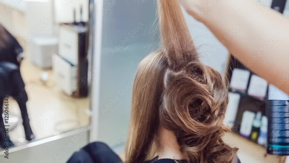 Hair stylist makes professional hairstyle of young woman in beauty studio