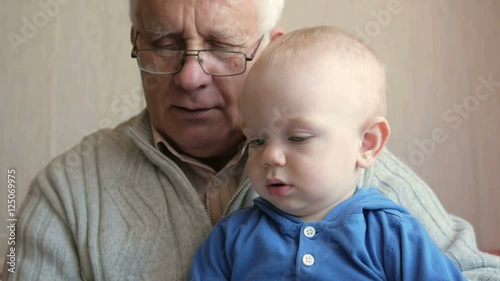 Grandpa with glasses reading a book beautiful baby. The child listens attentively to the tale. The boy about a year.
