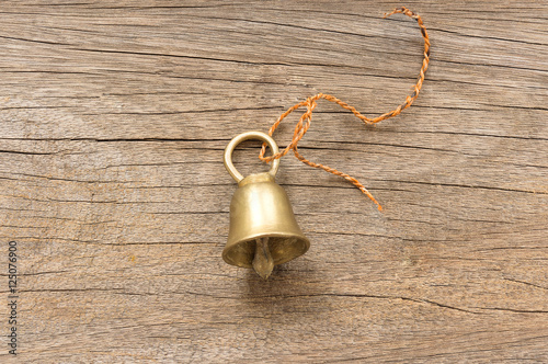 Golden bell with a rope tied to a loop. Placed on a wooden floor.