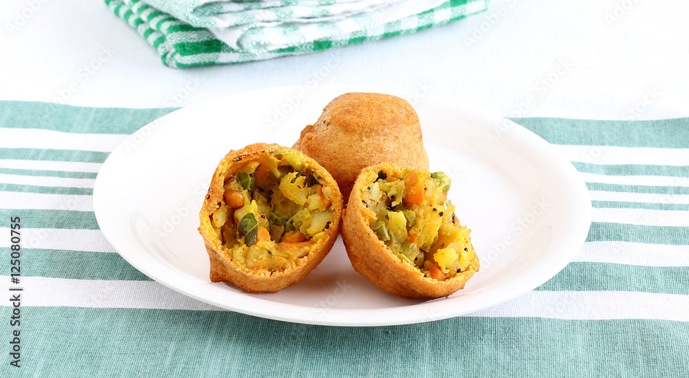 Indian vegetarian food aloo vada, broken into two halves, a traditional and popular snack, made from deep frying portions of chickpea flour, vegetables and mashed potato batter. Indian vegetarian food aloo vada, broken into two halves, a traditional and popular snack, made from deep frying portions of chickpea flour, vegetables and mashed potato batter.