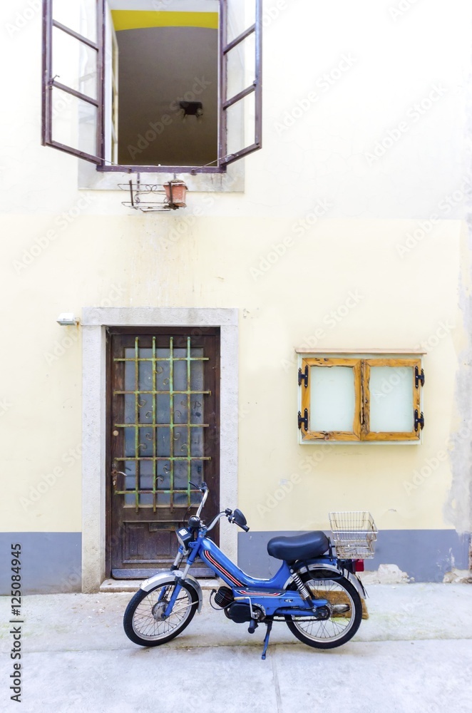 Traditional old Krk town architecture. View of door and open window and old tomos retro automatic motorcycle parked outside at the medieval ancient capital centre.