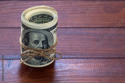 tied with a rope roll of hundred dollar bills on dark blurred wood background photo