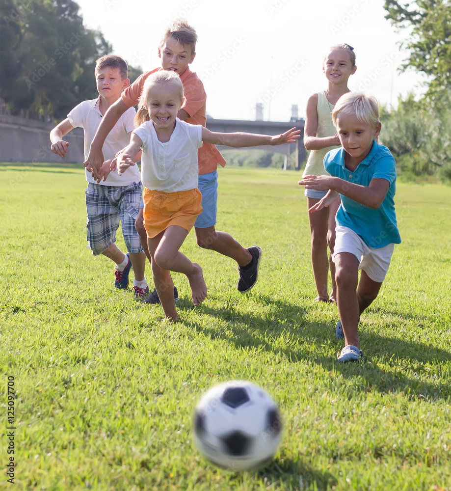 Group of cheerful kids playing football together on green lawn i