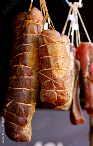 Smoked ham meat roasted sliced barbecue pork ribs in a traditional way hanging on dark background