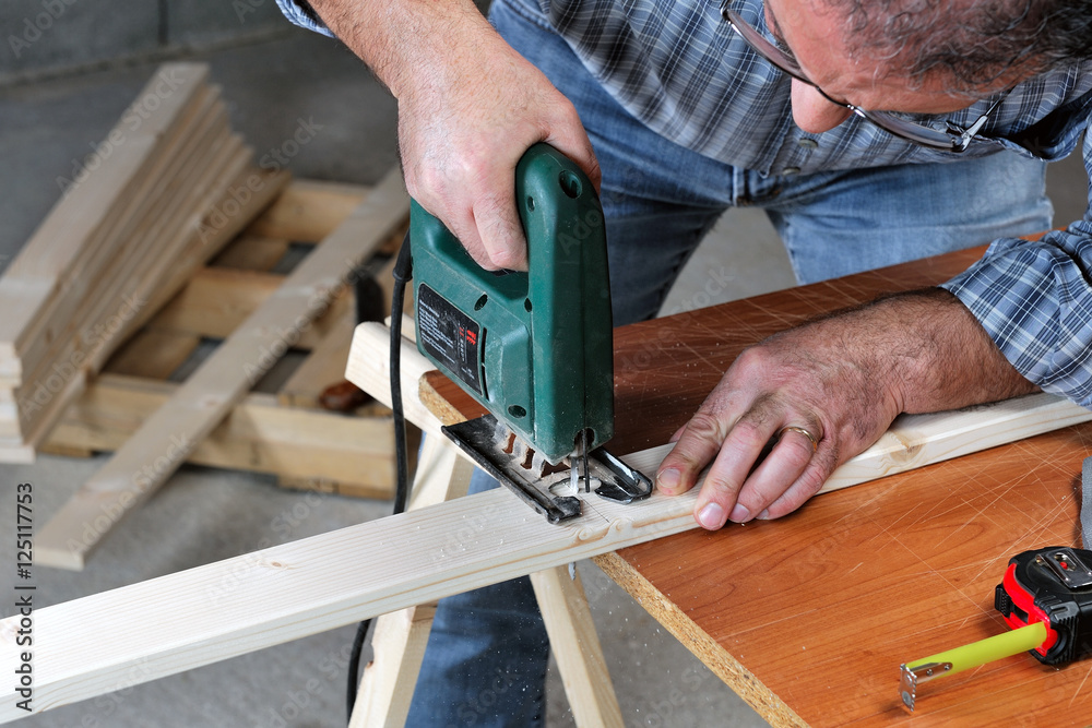 Adult artisan performs cutting with an electric saw of a strip of wood to manufacture a product. Adult artisan performs cutting with an electric saw of a strip of wood to manufacture a product.