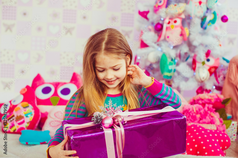 Little girl adjusts her hair while looking at violet present box Little girl adjusts her hair while looking at violet present box