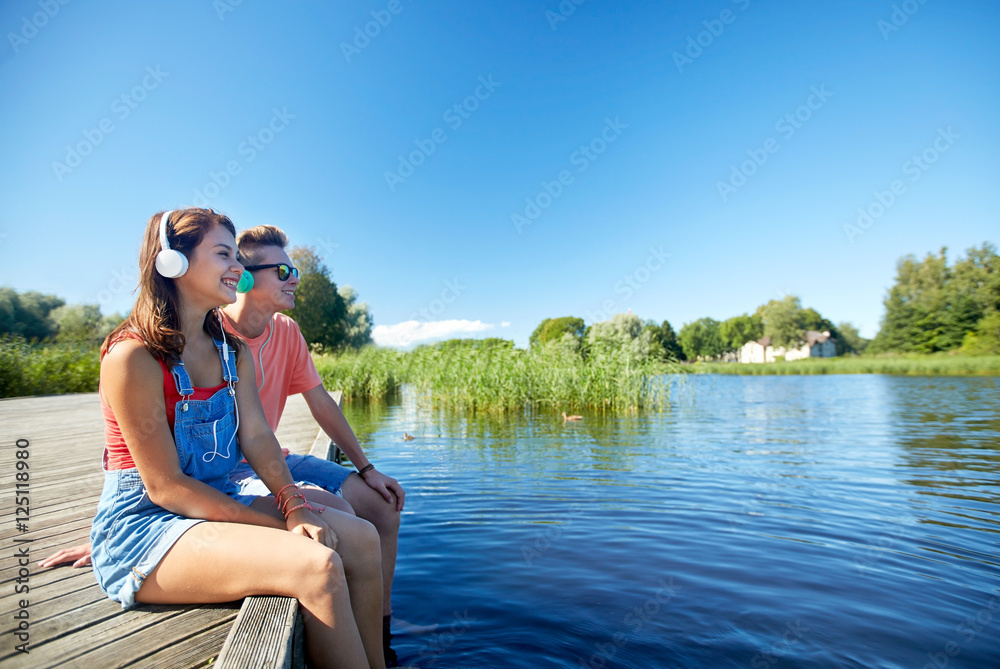 happy teenage couple with earphones on river berth