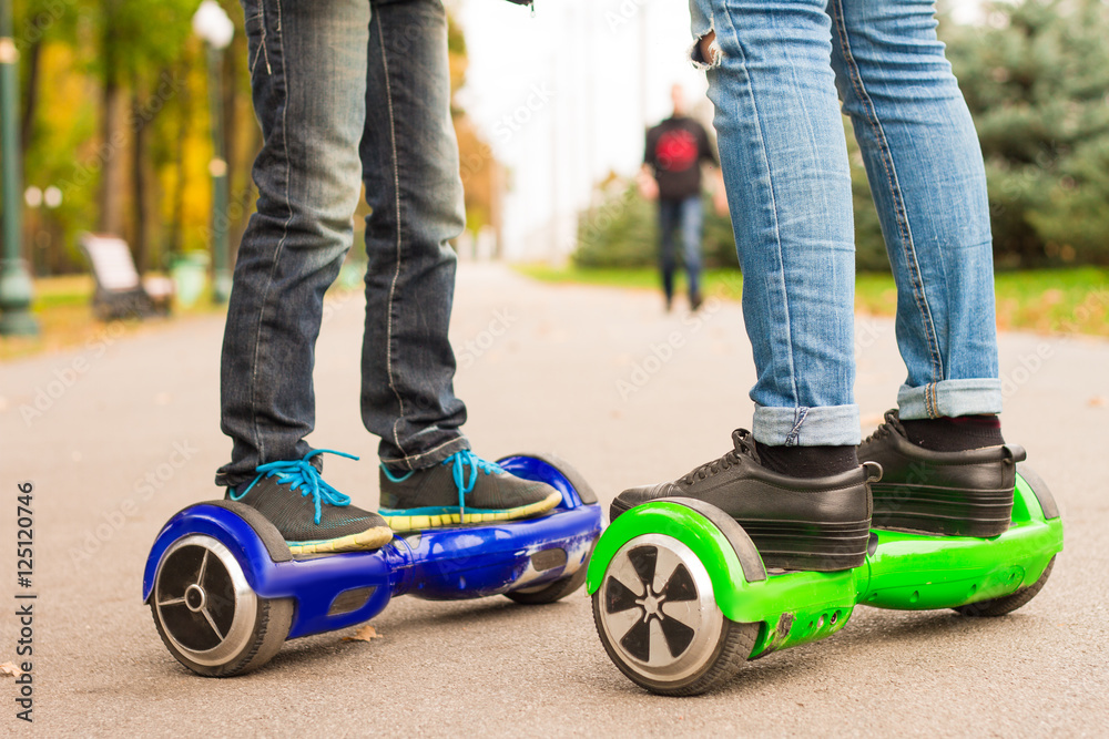 Fototapeta premium Feet of girl and boy riding electric mini segway outdoors in park
