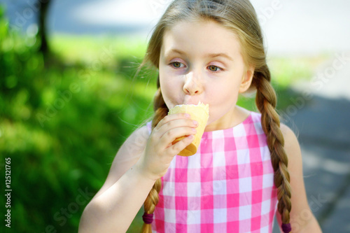 Adorable little girl eating tasty ice cream on summer day