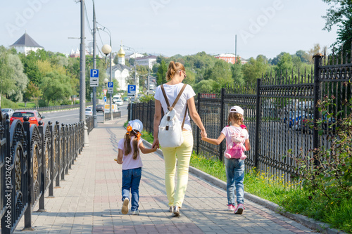 Mother and two daughters are on the sidewalk along the road