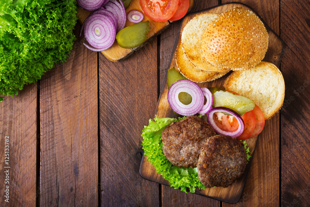 Ingredients for a sandwich - hamburger burger with beef, pickles, tomato and red onion on wooden background. Top view Ingredients for a sandwich - hamburger burger with beef, pickles, tomato and red onion on wooden background. Top view