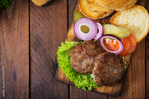 Ingredients for a sandwich - hamburger burger with beef, pickles, tomato and red onion on wooden background. Top view