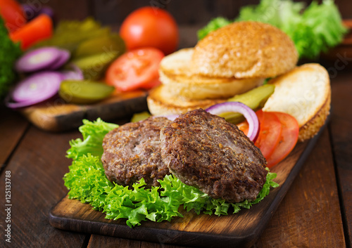 Ingredients for a sandwich - hamburger burger with beef, pickles, tomato and red onion on wooden background.