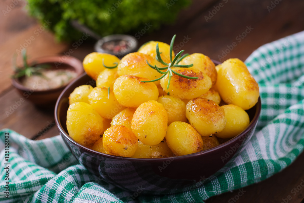 Baked potatoes with rosemary and pepper in a bowl on wooden background Baked potatoes with rosemary and pepper in a bowl on wooden background