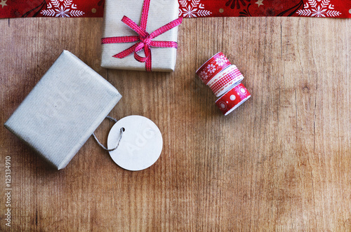 Christmas presents with red tied bow, label and ribbon laid on a wooden table background. Top view and copy space