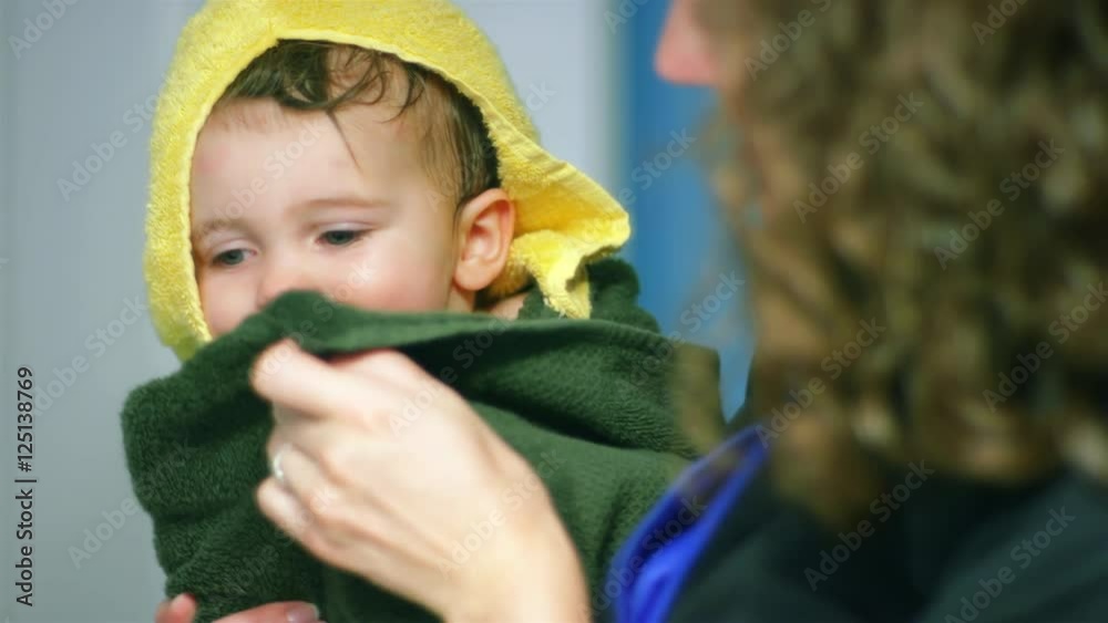 Adorable little boy wrapped in a towel as his mom dries off his face Adorable little boy wrapped in a towel as his mom dries off his face