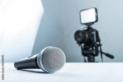 A wireless microphone lying on a white table against the background of the DSLR camera to led light.