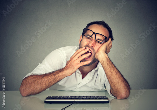Fotografija Sleepy worker man working on computer yawning