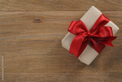 brown gift box with red ribbon bow on wooden oak table from above