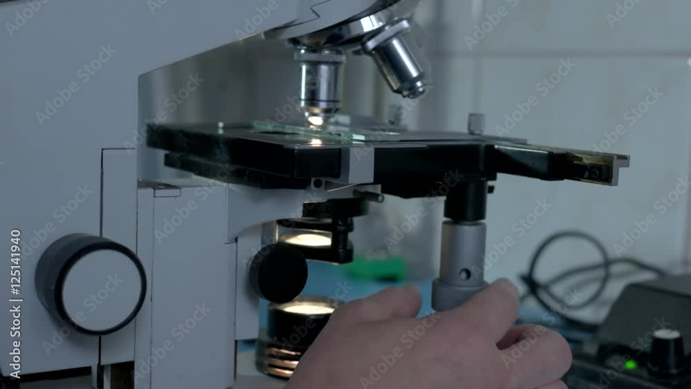 Side view of microscope. Hand touching scientific equipment. Be careful with new device. Research in medical lab. Side view of microscope. Hand touching scientific equipment. Be careful with new device. Research in medical lab.