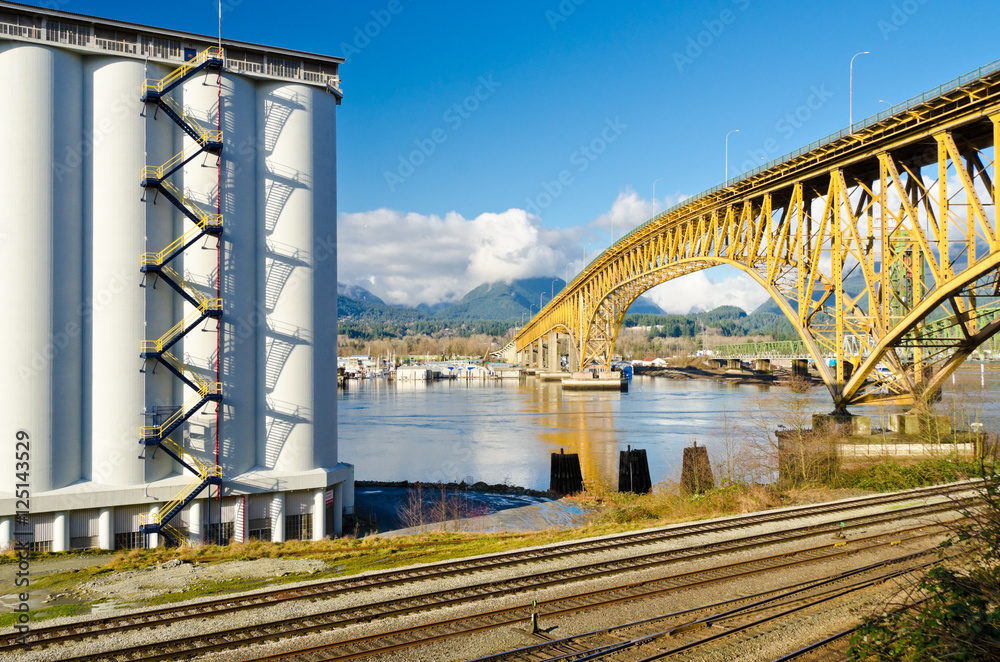 Naklejka premium Industrial Building over empty railways and nice yellow bridge across the inlet in Vancouver, Canada.