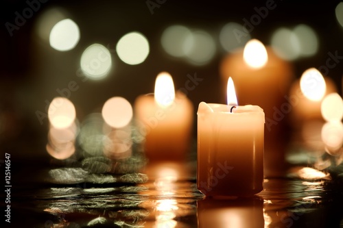 Burning candle with reflection against candlelight background photo