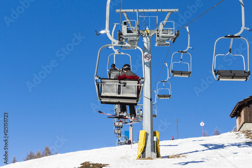 skiers on chairlift with snowy mountains in the background