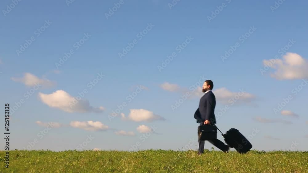 Businessman with suitcase in a field on the background of blue sky Businessman with suitcase in a field on the background of blue sky