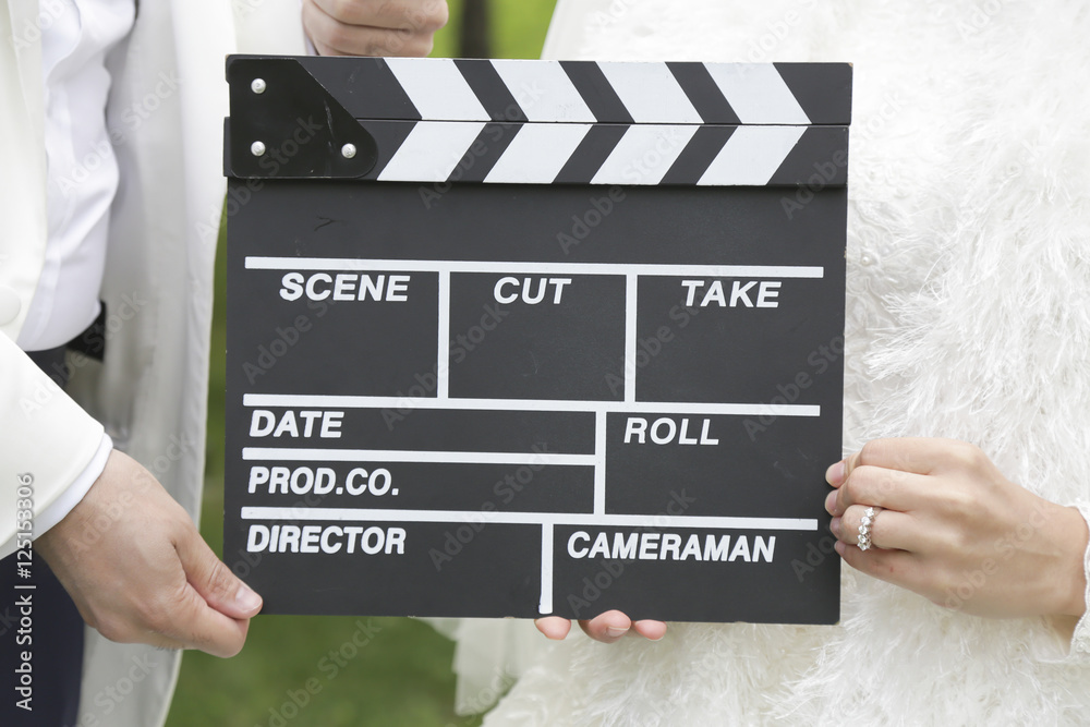 Obraz premium Happy beautiful bride and groom, woman holds clapper board, cinema board