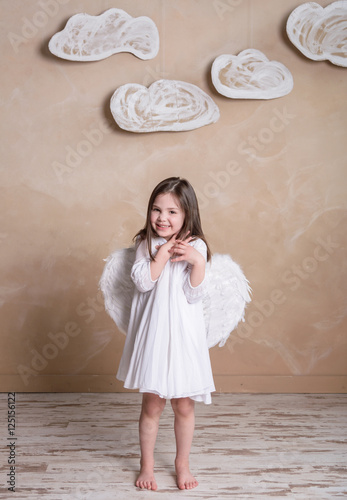 little angel girl in white dress with white wings under the clouds