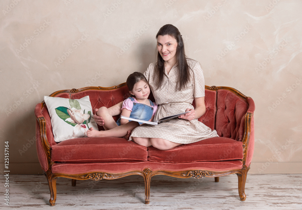 Mother and daughter reading book together on the red sofa Mother and daughter reading book together on the red sofa