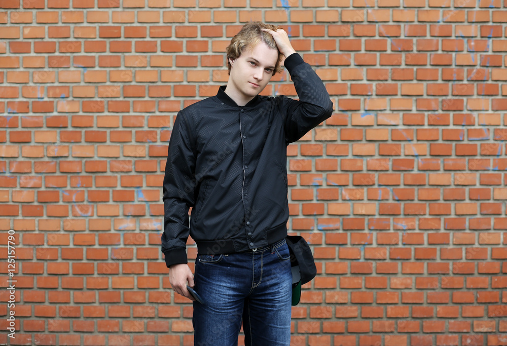 Portrait of attractive teenage boy standing in front of a brick wall. Portrait of attractive teenage boy standing in front of a brick wall.