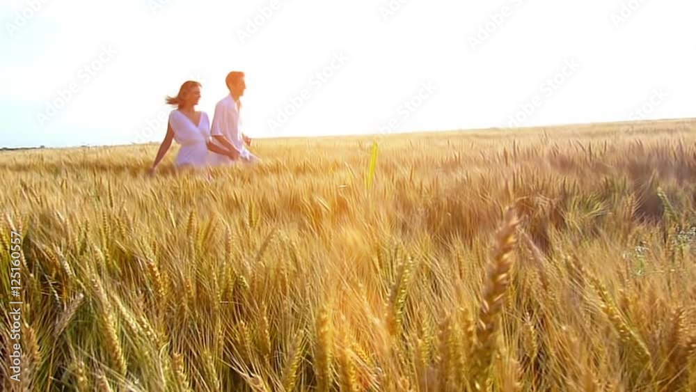 Happy, young couple running across the wheat field, summer season , sunset light.High speed camera, slow motion, flare light Happy, young couple running across the wheat field, summer season , sunset light.High speed camera, slow motion, flare light