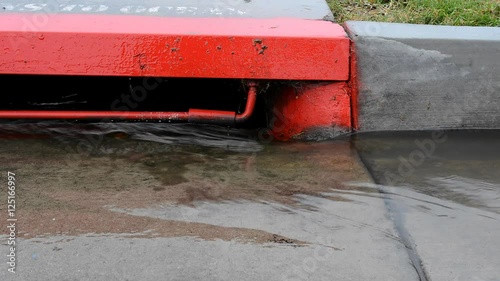 Rain creates water runoff along the side of a street, which drains into a city sewer system that leads to the ocean. Video is looped for unlimited duration. .