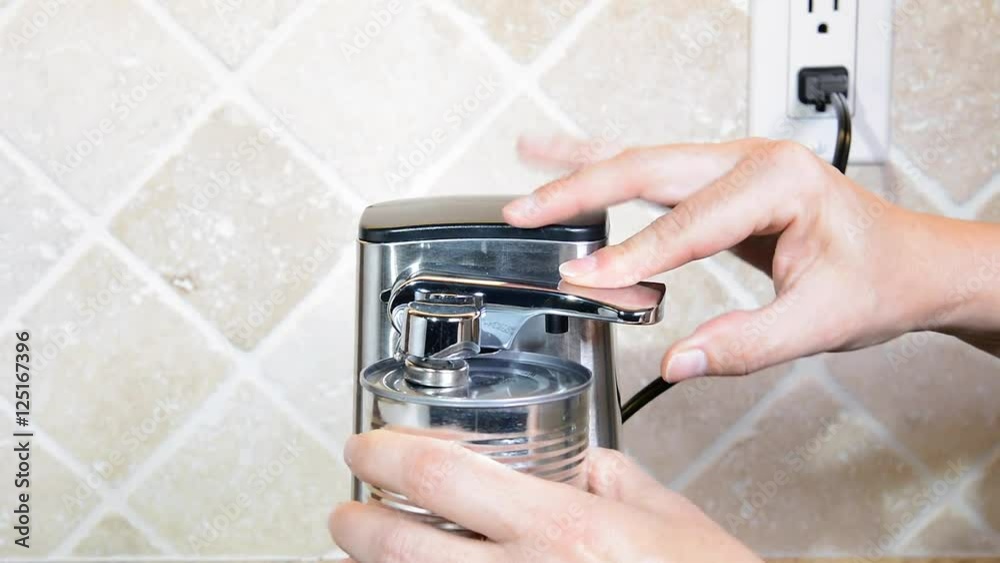A person uses an electronic can opener to open a can of sauce and remove it for cooking. A person uses an electronic can opener to open a can of sauce and remove it for cooking.