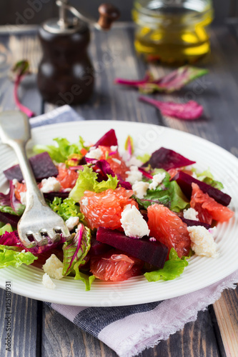 Salad of beets, lettuce, beetroot leaves, grapefruit and feta cheese on the old wooden background. Selective focus.