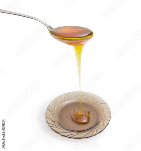 Spoon with honey above glass saucer on a light background