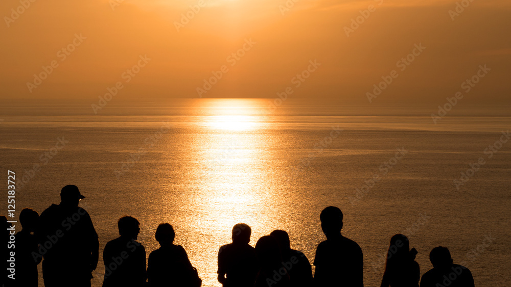 Silhouette of group of young people, friends, team standing enjoying together see orange sky at sunset over sea ocean.
