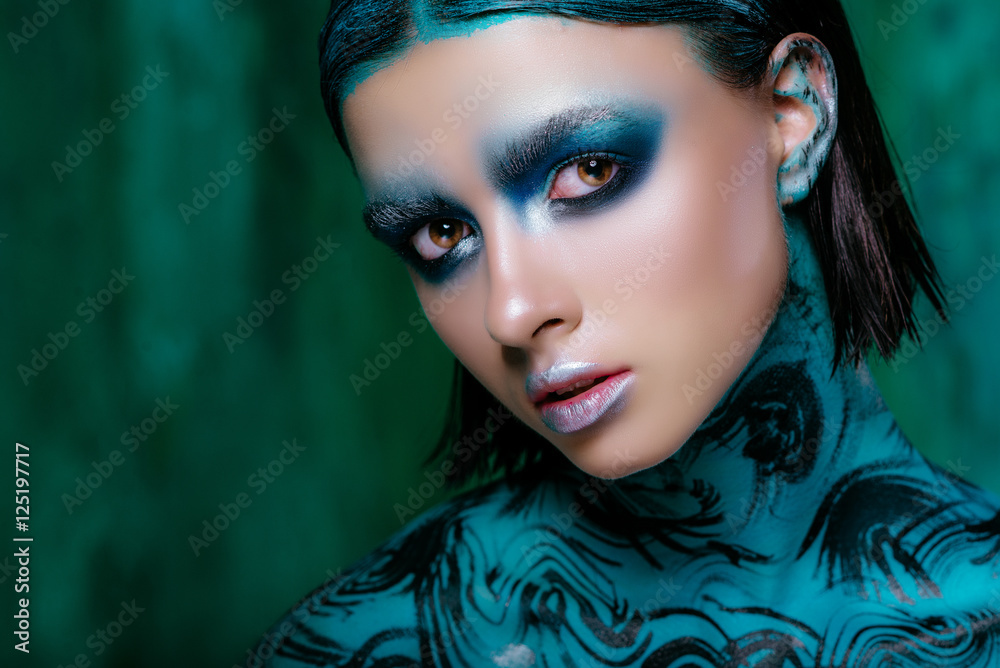 Art make-up in bright colors. Beautiful brunette girl in short hair posing in the studio on a turquoise background. Radiant skin Art make-up in bright colors. Beautiful brunette girl in short hair posing in the studio on a turquoise background. Radiant skin