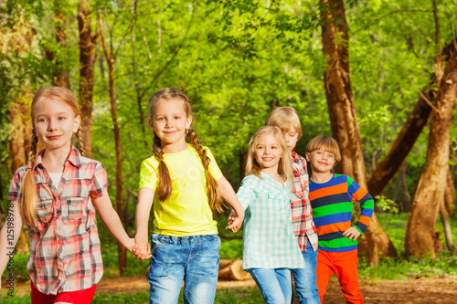 Happy friends walking in the forest holding hands