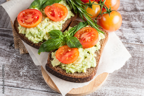 Avocado toast, cherry tomato on wooden background. Breakfast with toast avocado, vegetarian food, healthy diet concept.