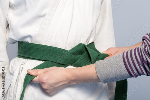 Hands of a parent who helps a child to tie a green belt for martial arts training